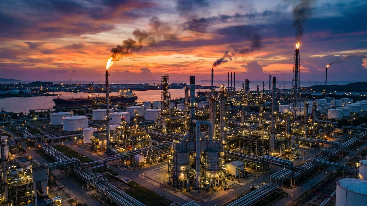 Oil refinery complex at dusk with flare stacks and tanker ships