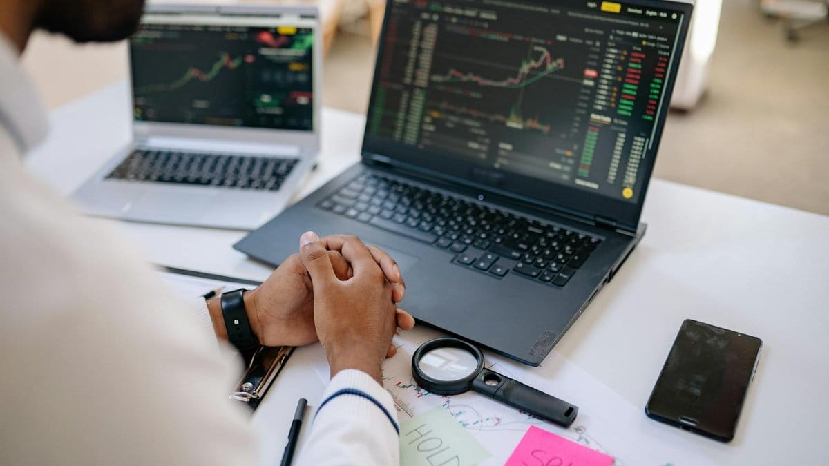 Business professional analyzing stock market charts on dual laptop screens