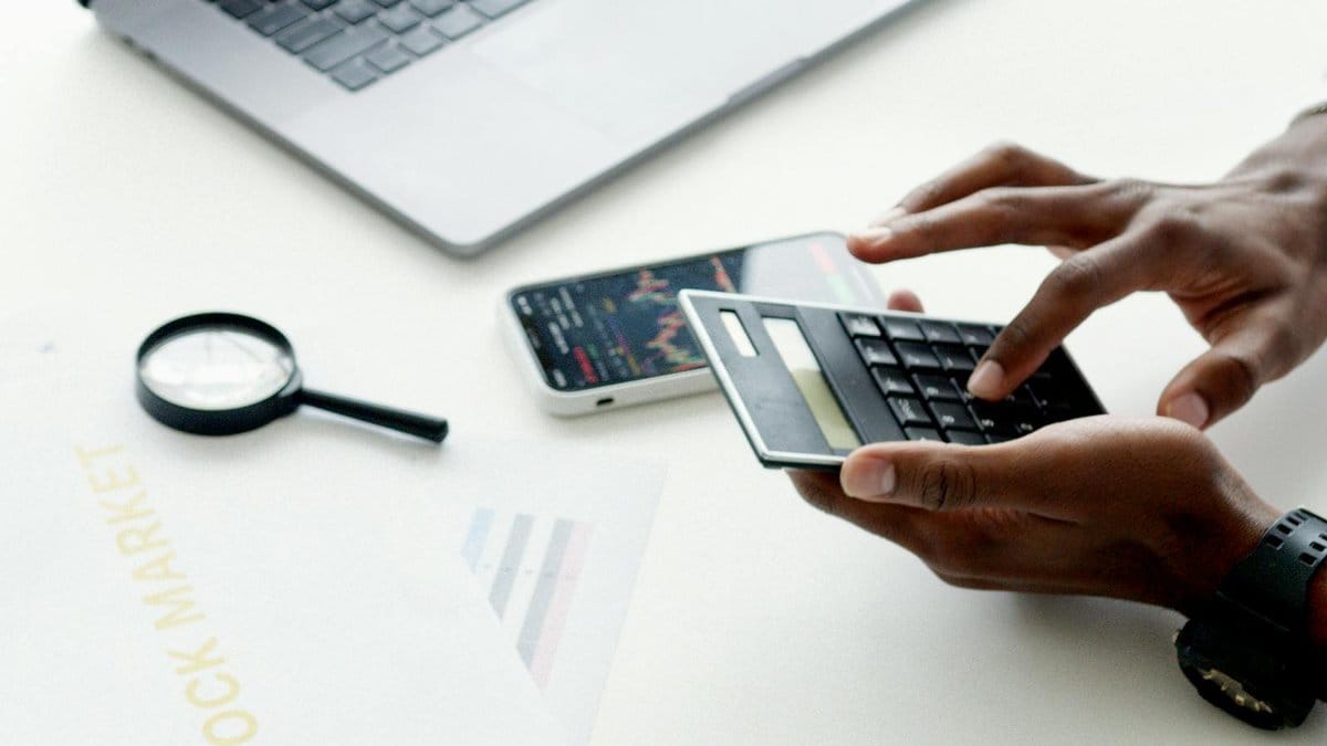Financial analyst reviewing stock market data on laptop with market charts in background