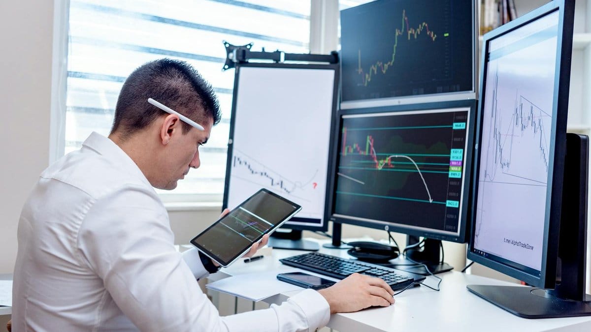 Financial analyst reviewing stock market data on multiple monitors