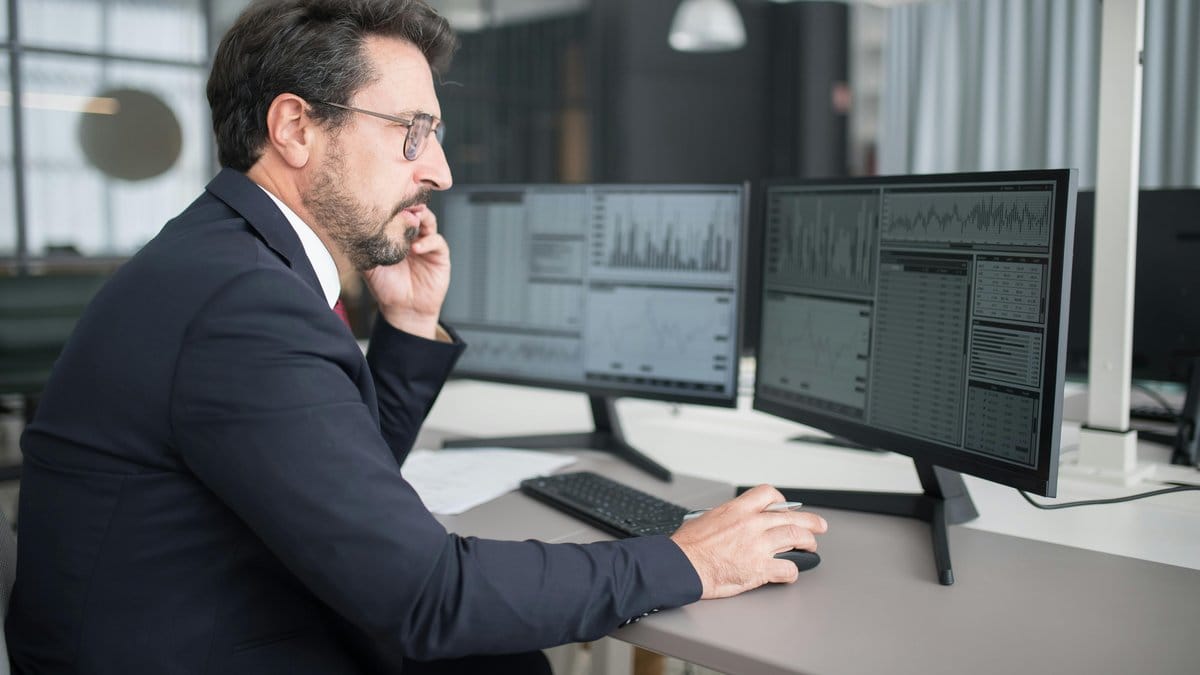 Financial analyst reviewing technology stock market data on multiple screens