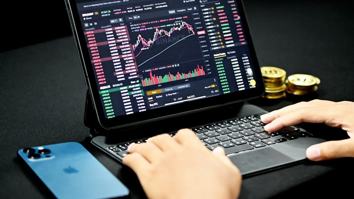 A trader analyzing cryptocurrency market data on a tablet and laptop screen