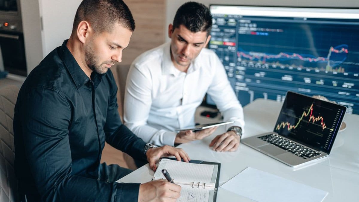 Two financial analysts reviewing economic data and market charts on digital devices