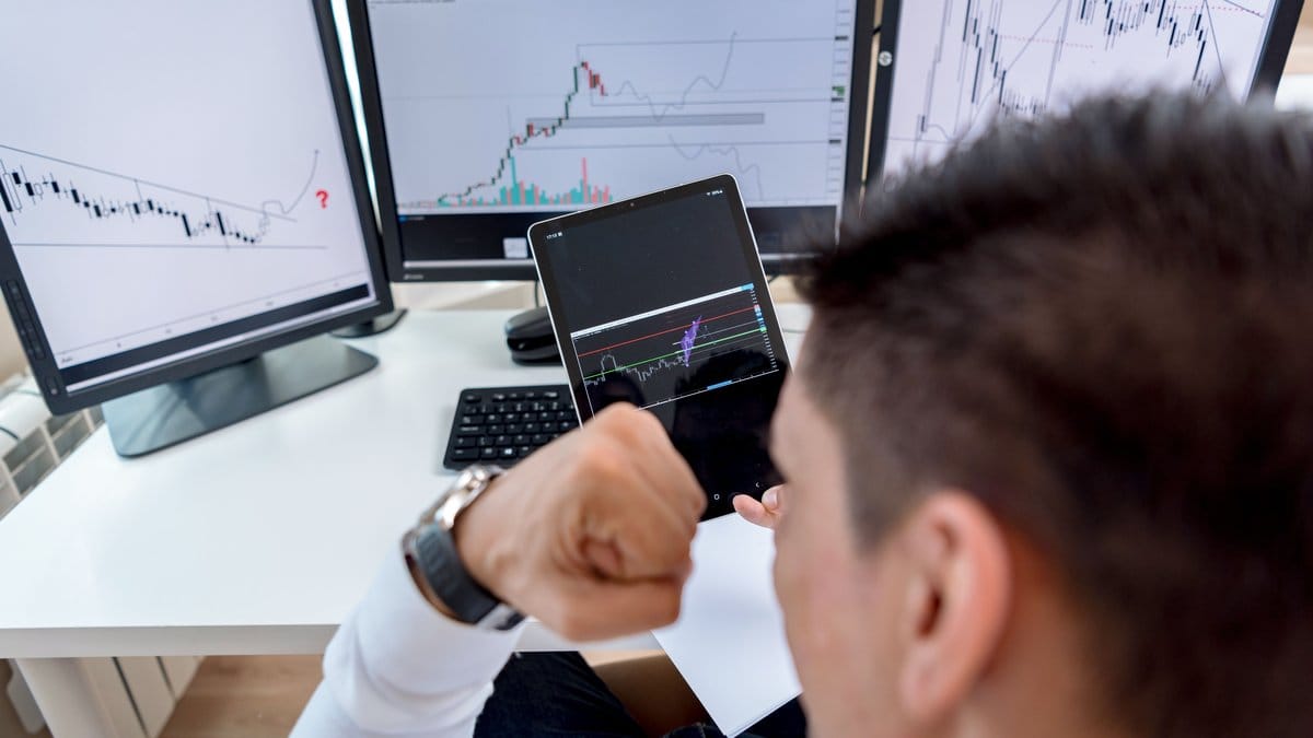 Trader monitoring multiple stock market screens and charts on tablet and desktop monitors