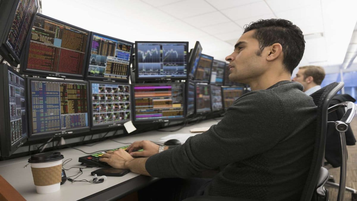 Financial market trader monitoring multiple screens displaying real-time stock data and market analytics