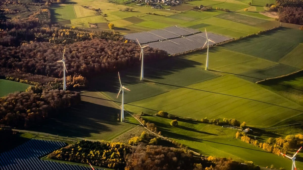 Solar panels and wind turbines in a rural landscape representing the renewable energy transition