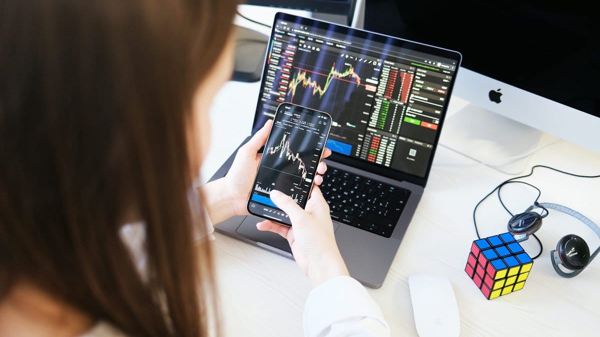 Investor monitoring financial market charts on a smartphone and laptop