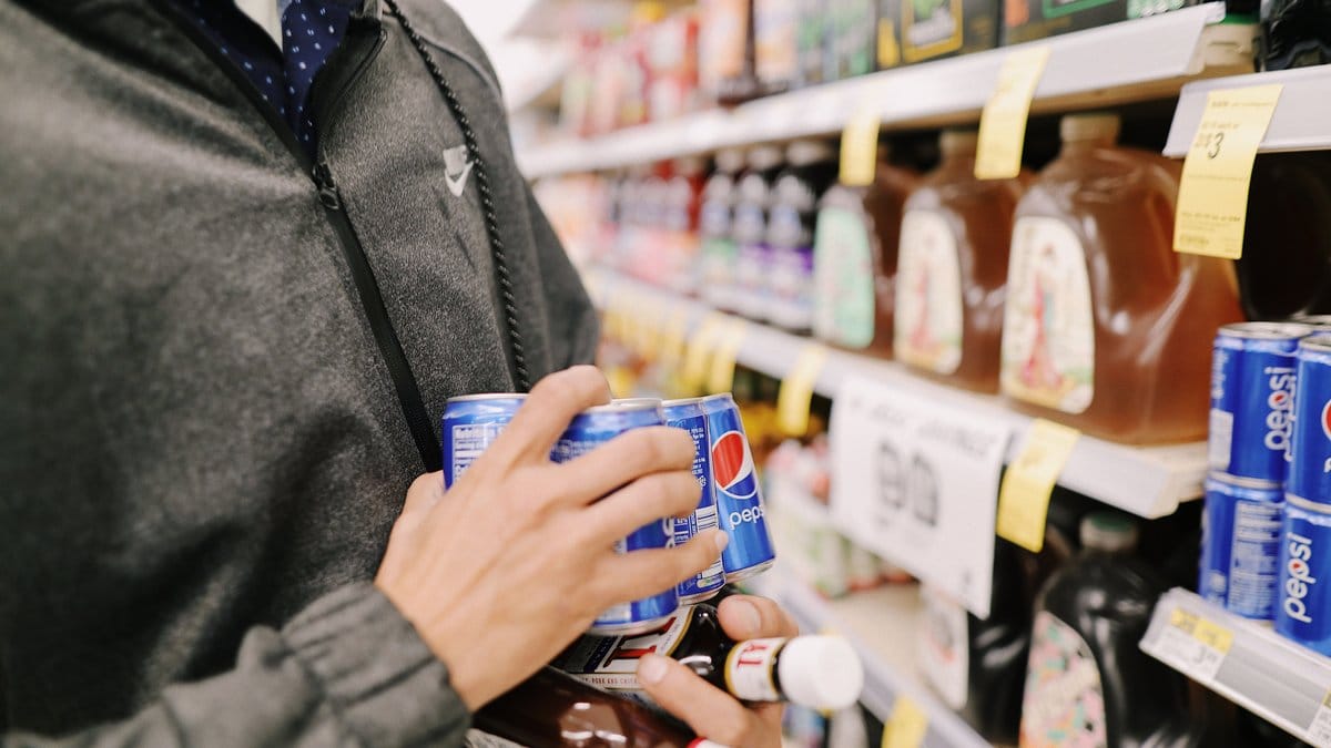A shopper selecting Pepsi products in a grocery-store beverage aisle