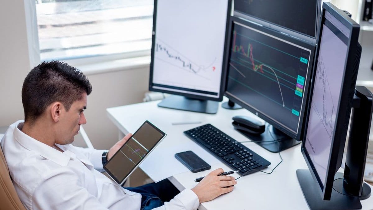 Financial analyst reviewing market performance data across multiple trading screens and tablet