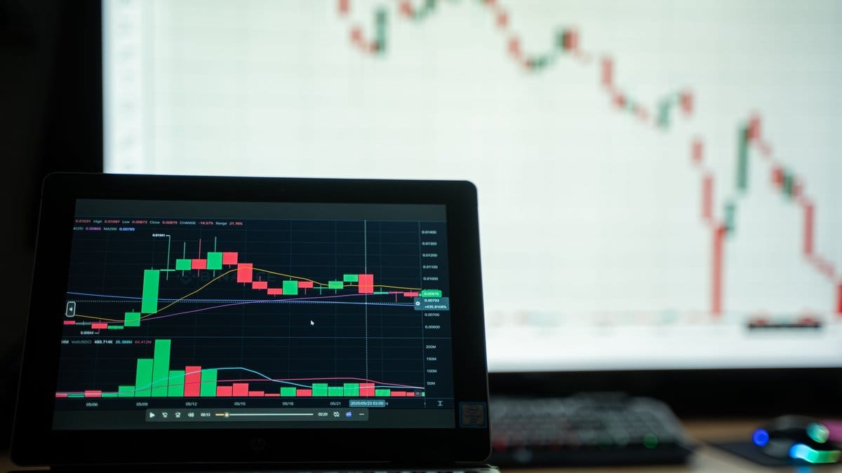 Laptop and monitor displaying stock market charts in a professional trading workspace