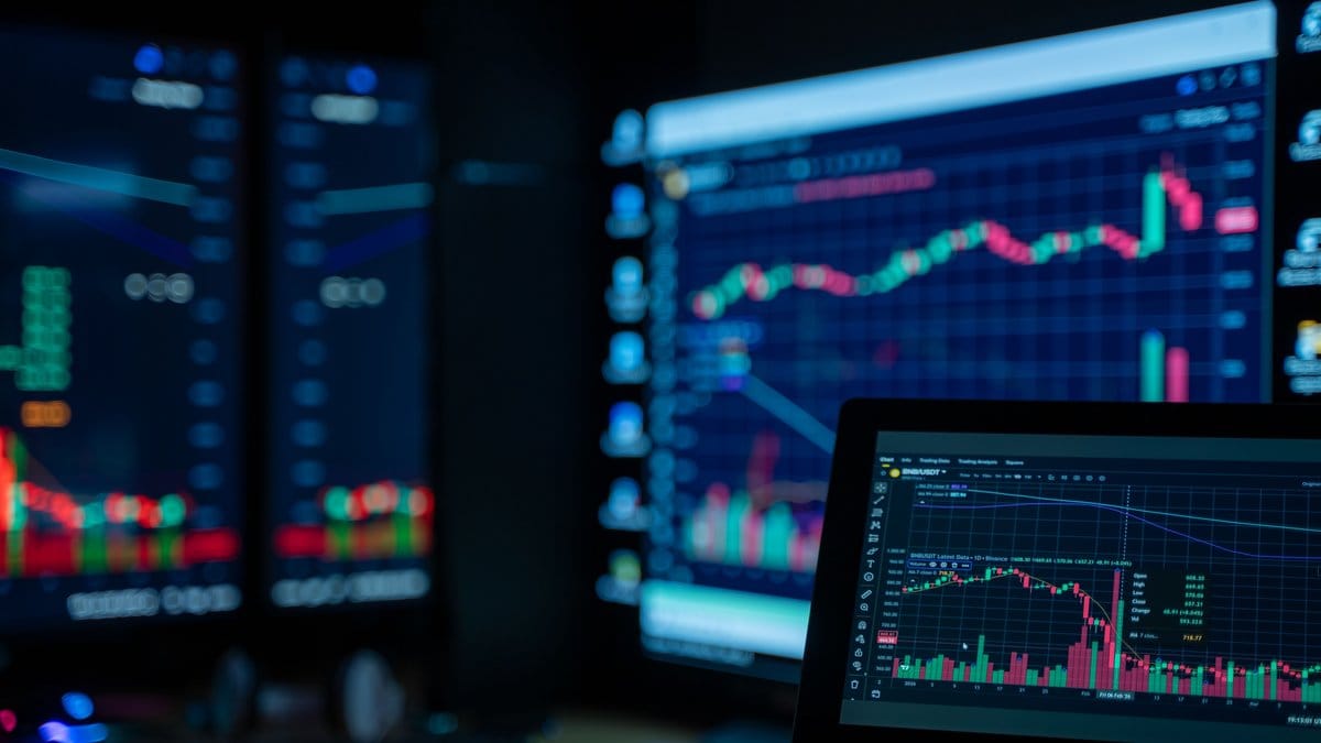 Multiple trading monitors displaying stock market charts and financial data for weekly market analysis