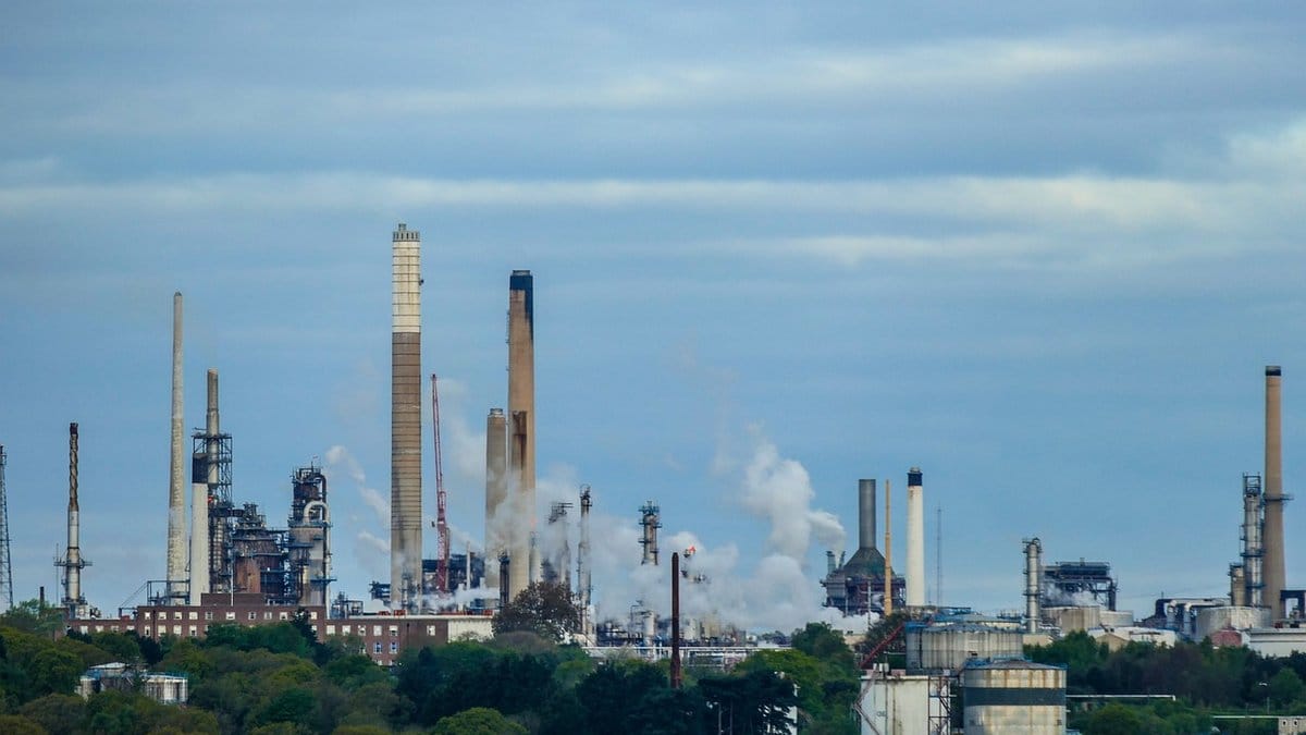 Industrial oil refinery with stacks and processing equipment beneath a blue sky