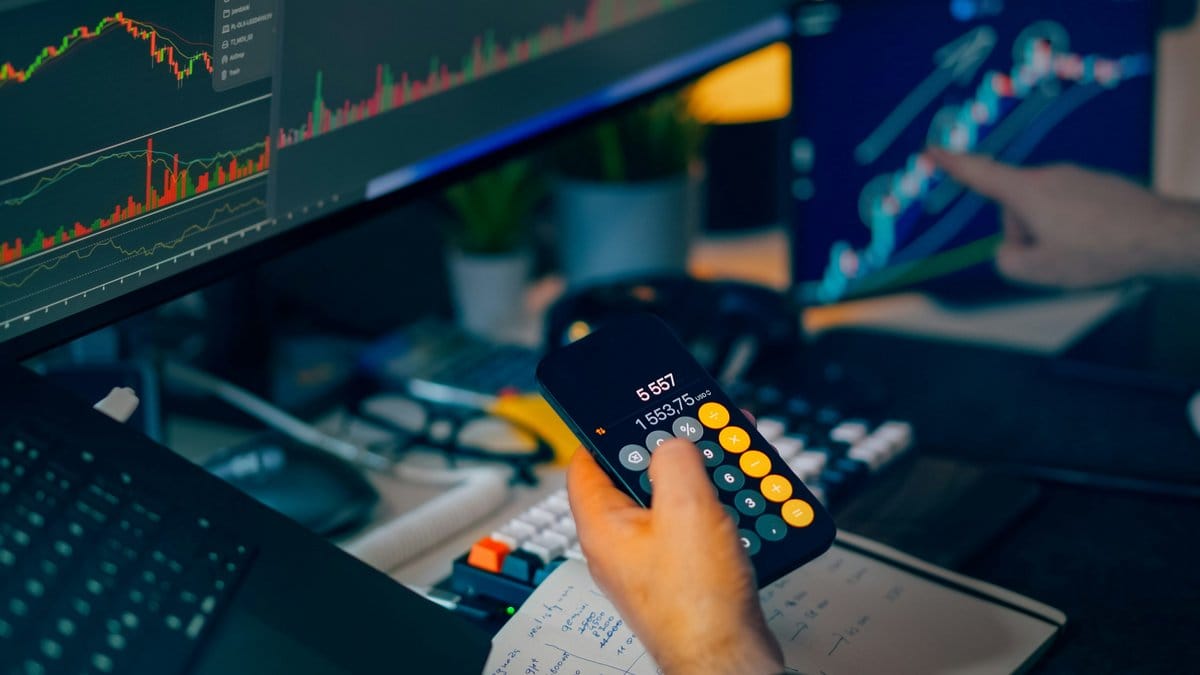 Market analyst reviewing stock charts and calculations on multiple trading screens