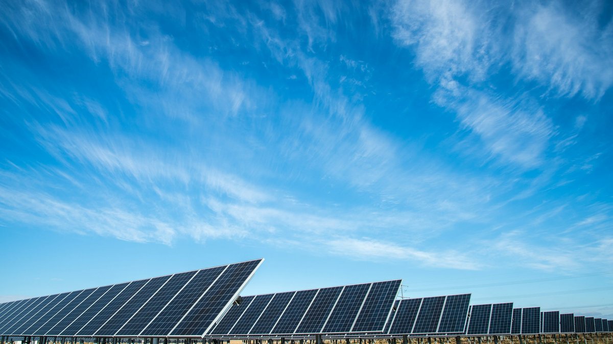 Utility-scale solar panel arrays beneath a bright blue sky with wispy clouds