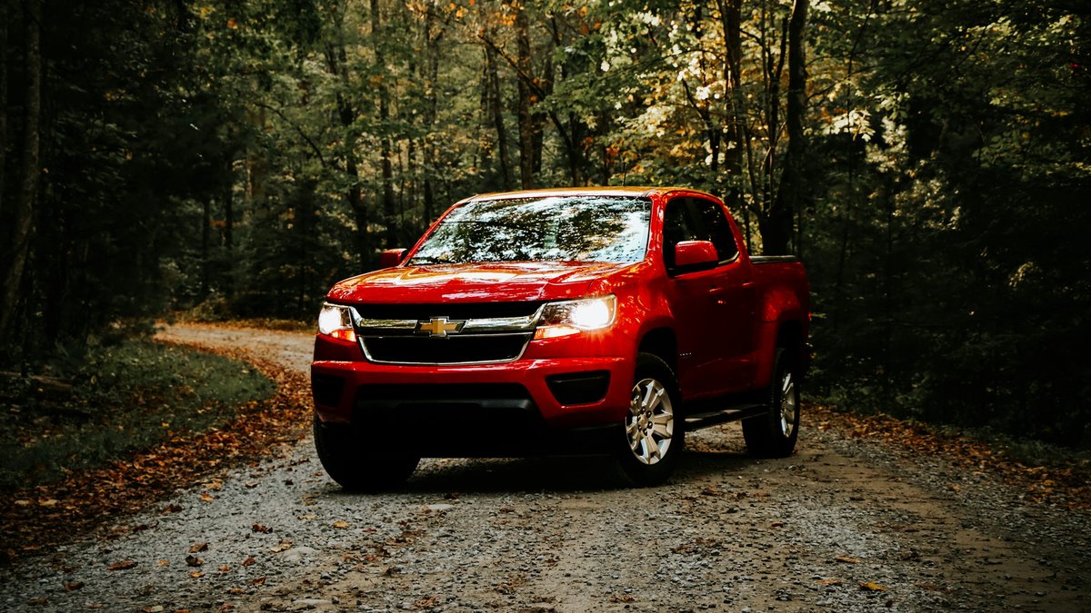 Red Chevrolet pickup truck parked on a forest road, illustrating General Motors' truck business