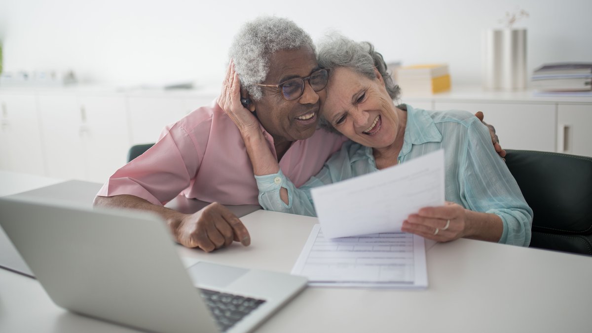 Senior couple reviewing retirement paperwork together beside a laptop