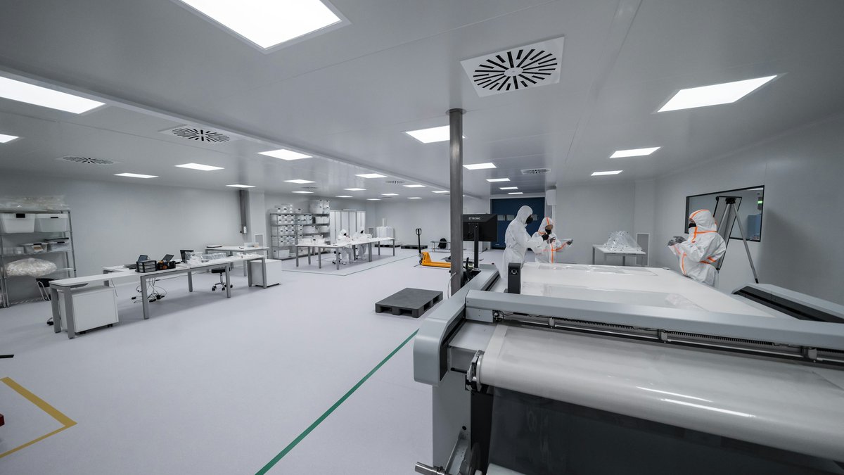 Workers in protective suits operate equipment in a bright industrial cleanroom.